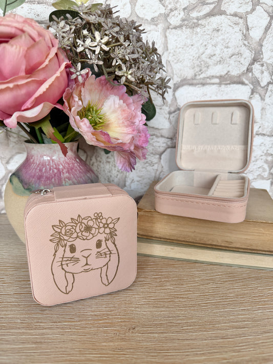 Pink jewelry case with a bunny design on a wooden surface with flowers in the background