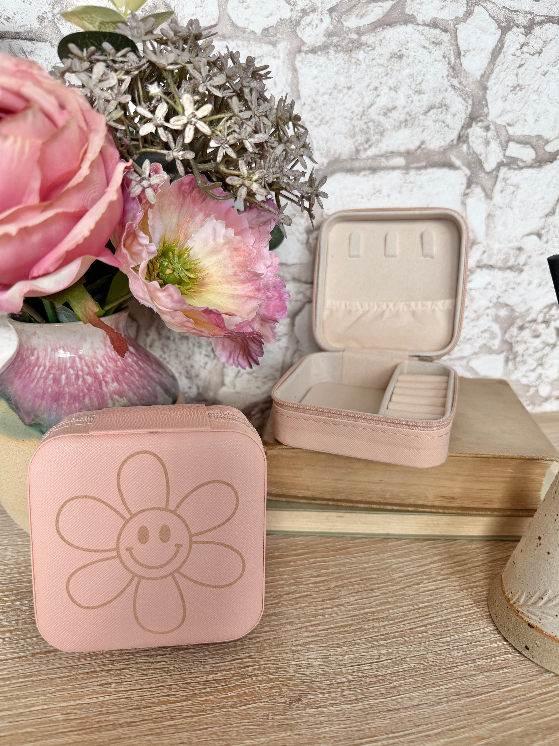 Pink jewelry case with flower design on a wooden surface with flowers in the background